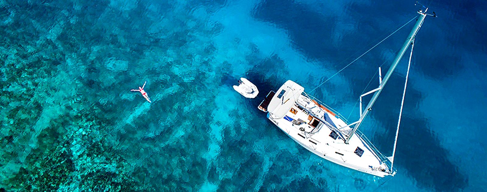 El velero fondeado sobre agua turquesa, visto desde el aire